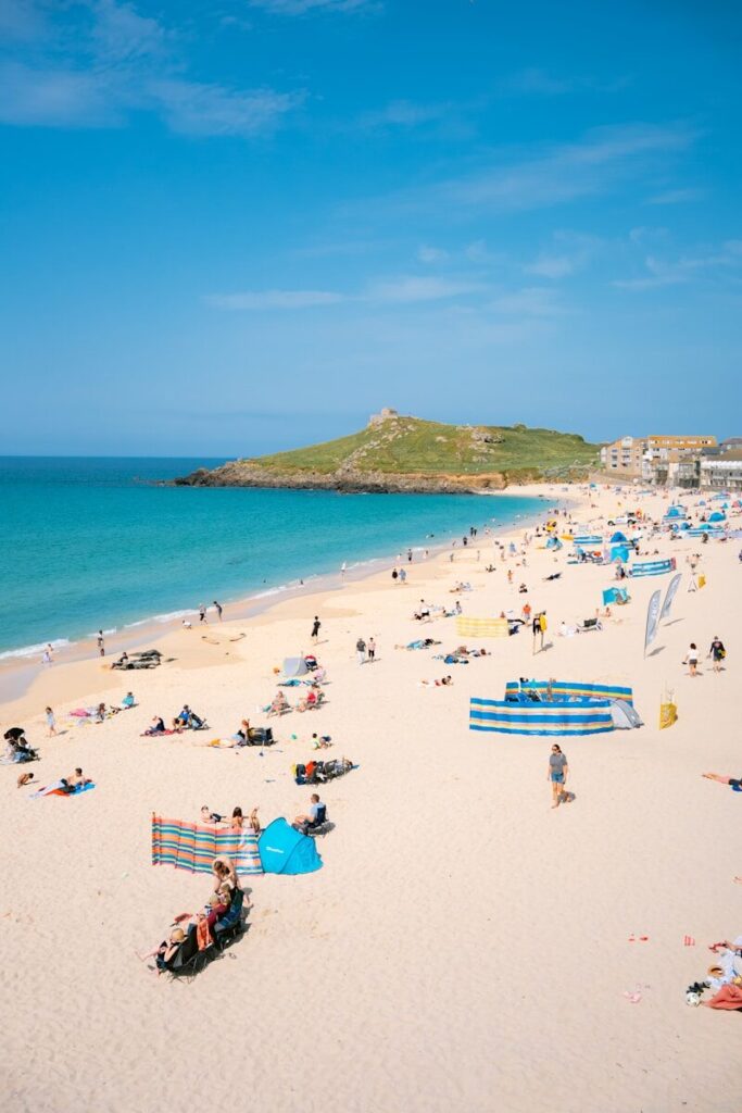 People relaxing on a crowded sandy beach with turquoise sea.