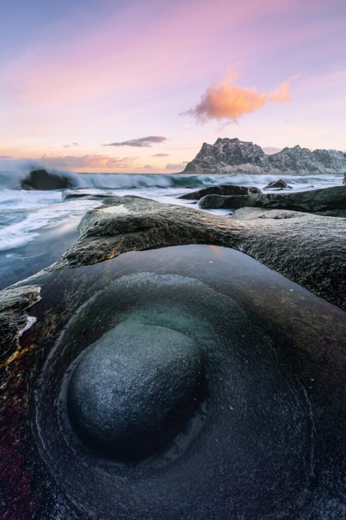 Rocky coastline with ocean waves and mountains at twilight.
